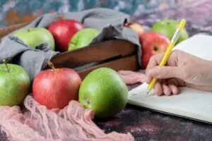 Image of person writing with apples on the table